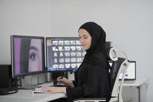 graphiste musulmane travaillant sur ordinateur à l'aide d'une tablette graphique et de deux moniteurs photo