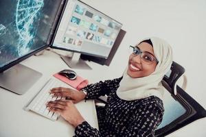 jeune femme d'affaires musulmane moderne afro-américaine portant un foulard dans un lieu de travail créatif et lumineux avec un grand écran. photo