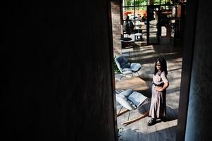 portrait de mode d'une femme afro-américaine en robe longue, bottes et lunettes de soleil à l'intérieur. photo