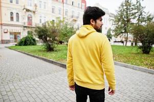 jeune hipster indien urbain dans un sweat-shirt jaune à la mode. un mec sud-asiatique cool porte un sweat à capuche dans la rue. photo