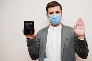 homme européen en tenue de soirée et masque facial, montre le passeport de la bosnie-herzégovine avec la main du panneau d'arrêt. verrouillage du coronavirus dans le concept de pays d'europe. photo