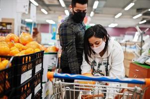 un couple asiatique porte un masque protecteur faisant ses courses ensemble dans un supermarché pendant la pandémie. choisissez des fruits de pomelo. photo