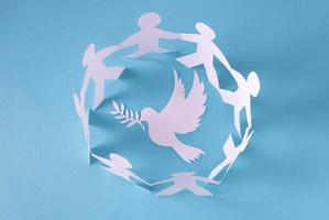 les gens découpés dans du papier sur fond bleu protègent la colombe de la paix.le concept de la journée mondiale de la paix photo