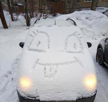 une voiture couverte de neige, avec une drôle de tête sur le capot. plaisirs d'hiver photo