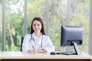 une belle femme médecin asiatique écrit quelque chose sur le papier alors qu'elle est assise et travaille dans une salle de bureau à l'hôpital dans le concept de soins de santé et de protection contre les coronavirus. photo