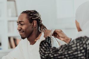 un jeune couple musulman passe un moment romantique à la maison tandis que la femme fait la coiffure de son mari, une femme portant des vêtements traditionnels du hijab islamique du soudan. photo