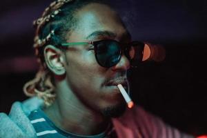 Afro-américains fumant un cigare, dans les lumières de la ville en arrière-plan photo