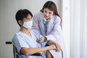 une femme médecin asiatique explique et suggère des informations avec un homme patient assis sur un fauteuil roulant. ils portent un masque médical lorsqu'ils parlent ensemble à l'hôpital. photo