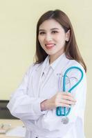 jeune belle femme médecin asiatique debout avec les bras croisés heureux et sourire à l'hôpital. portant une robe blanche et un stéthoscope photo