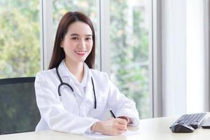 une belle femme médecin asiatique écrit quelque chose sur le papier et travaille joyeusement à l'hôpital. photo