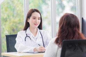 une femme asiatique qui porte un manteau médical et un stéthoscope s'entretient avec une patiente pour consulter et suggérer des informations sur les soins de santé à l'hôpital. photo