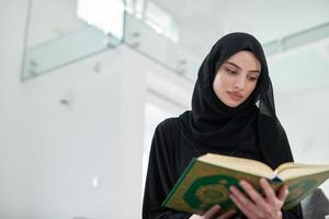 portrait de jeune femme musulmane lisant le coran dans une maison moderne photo
