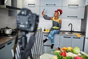 femme afro-américaine filmant son blog diffusé sur des aliments sains dans la cuisine à domicile. elle fait selfie au téléphone. photo