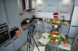 femme afro-américaine filmant son blog diffusé sur des aliments sains dans la cuisine à domicile. elle tient un chou. photo