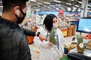 un couple asiatique porte un masque protecteur faisant ses courses ensemble dans un supermarché pendant la pandémie. peser l'ananas. photo