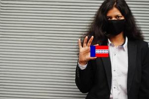 une femme asiatique en tenue de soirée et un masque de protection noir tiennent le drapeau des tuamotu à portée de main sur fond gris. coronavirus au concept de pays. photo