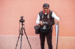 jeune vidéaste afro-américain professionnel tenant une caméra professionnelle avec un équipement professionnel. caméraman afro portant du duraq noir faisant des vidéos. photo