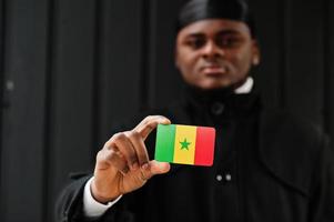 l'homme africain porte du durag noir tient le drapeau du sénégal à la main isolé sur fond sombre. photo