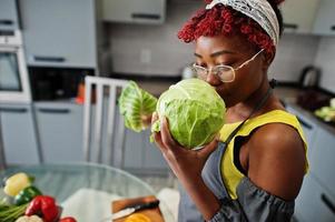 femme afro-américaine préparant des aliments sains à la cuisine à domicile. elle tient un chou.