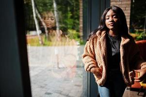 une femme afro-américaine à la mode porte une veste debout près de la fenêtre. photo