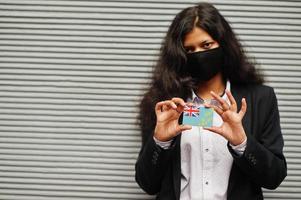 une femme asiatique en tenue de soirée et un masque de protection noir tiennent le drapeau tuvalu à portée de main sur fond gris. coronavirus au concept de pays. photo