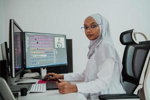 jeune femme d'affaires musulmane moderne afro-américaine portant un foulard dans un lieu de travail créatif et lumineux avec un grand écran. photo