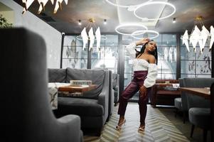 belle femme afro-américaine en blouse blanche et pantalon en cuir rouge pose au restaurant. photo