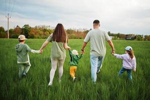 dos de parents marchant avec trois enfants s'amusant ensemble au pré. photo