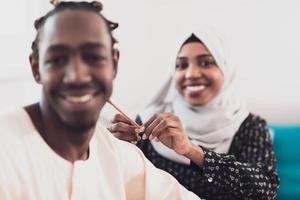 un jeune couple musulman passe un moment romantique à la maison tandis que la femme fait la coiffure de son mari, une femme portant des vêtements traditionnels du hijab islamique du soudan. photo