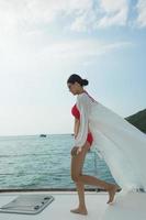 belle femme asiatique à la peau bronzée de race mélangée marchant le long de yachts de luxe dans l'océan profond, fille de lunettes de soleil bikini rouge se présentant comme mannequin dans la jetée d'amarrage sous le ciel bleu d'été en vacances photo