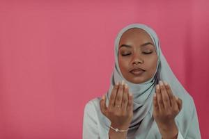 la femme musulmane africaine moderne fait la prière traditionnelle à dieu, garde les mains dans le geste de prière, porte des vêtements blancs traditionnels, a une expression faciale sérieuse, isolée sur fond rose en plastique photo