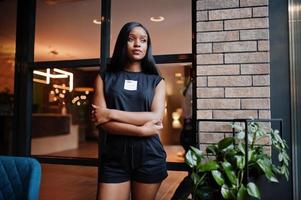 femme afro-américaine féministe à la mode vêtue d'un t-shirt et d'un short noirs, posée au restaurant. photo