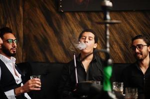 un groupe de beaux gangsters rétro bien habillés passe du temps au club, fumant du narguilé. fête de la mafia masculine multiethnique au restaurant. photo