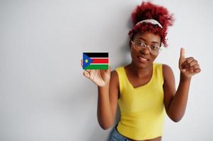 femme africaine aux cheveux afro, porter un maillot et des lunettes jaunes, tenir le drapeau sud-soudanais isolé sur fond blanc, montrer le pouce vers le haut. photo