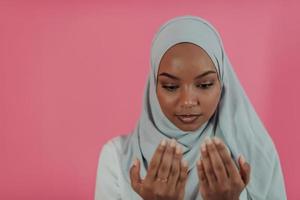 la femme musulmane africaine moderne fait la prière traditionnelle à dieu, garde les mains dans le geste de prière, porte des vêtements blancs traditionnels, a une expression faciale sérieuse, isolée sur fond rose en plastique photo