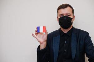 l'homme européen porte un masque formel noir et protège le visage, tient la carte du drapeau de la france isolée sur fond blanc. concept de pays europe coronavirus covid. photo