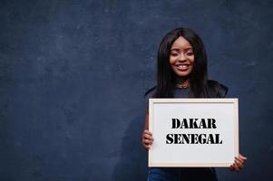 une femme africaine tient un tableau blanc avec inscription dakar sénégal. concept de ville la plus peuplée d'afrique. photo