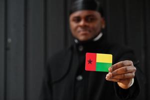 un homme africain porte du durag noir tient le drapeau de la guinée-bissau à la main isolé sur fond sombre. photo