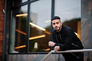 portrait d'un homme à la barbe arabe élégant portant un col roulé gris et un jaket noir. mec modèle arabe. photo