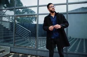 l'entrepreneur du moyen-orient porte un manteau noir et une chemise bleue, des lunettes contre la cigarette de l'immeuble de bureaux. photo