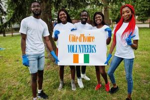 un groupe de volontaires africains heureux tient en blanc avec le drapeau de la côte d'ivoire dans le parc. concept de volontariat, de charité, de personnes et d'écologie des pays africains. photo