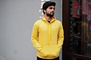 jeune homme indien hipster urbain dans un sweat-shirt jaune à la mode. un gars sud-asiatique cool porte un sweat à capuche. photo