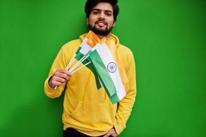 un jeune indien hipster urbain dans un sweat-shirt jaune à la mode tient des drapeaux de l'inde dans les mains. un gars sud-asiatique cool porte un sweat à capuche isolé sur fond vert. photo