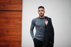 portrait d'un homme à la barbe arabe élégant portant un col roulé gris et un jaket noir. mec modèle arabe. photo