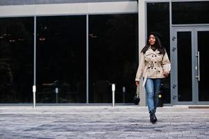 une femme afro-américaine à la mode porte un béret et un manteau avec un sac à main posant à l'extérieur. photo