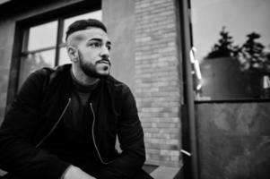 portrait d'un homme à la barbe arabe élégant portant un col roulé gris et un jaket noir. modèle arabe guy squat. photo