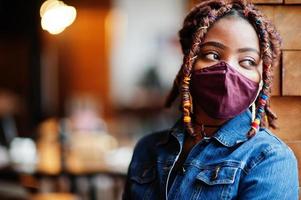 femme afro-américaine élégante avec des cheveux afro dreadlocks, porter une veste en jean et un masque de protection du visage au restaurant. nouvelle vie normale après l'épidémie de coronavirus.