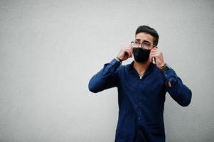 un entrepreneur du moyen-orient porte un masque noir et des lunettes contre un mur blanc. nouvelle vie normale après la pandémie de coronavirus. photo