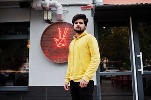 jeune homme indien hipster urbain dans un sweat-shirt jaune à la mode. un gars sud-asiatique cool porte un sweat à capuche. photo