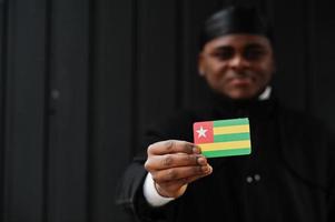 l'homme africain porte du durag noir tient le drapeau togo à la main isolé sur fond sombre. photo